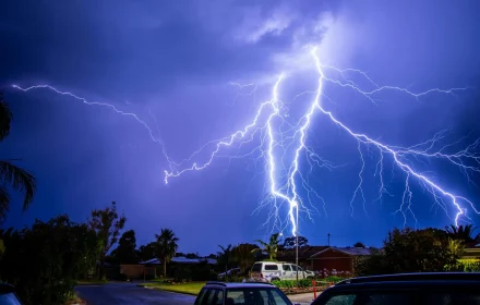 Dramatic lightning strike illuminating a residential area during a nighttime thunderstorm.